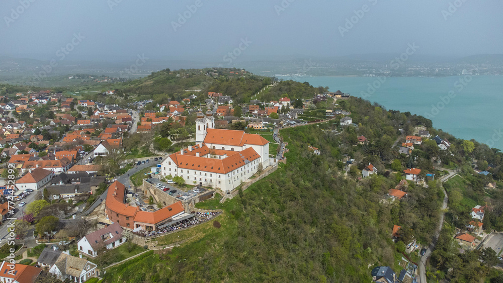 Tihanyi Bencés Apátság, or the Benedictine Abbey of Tihany, is a historic monastery located in Tihany, Hungary, perched on a scenic hill overlooking Lake Balaton captured from a drone