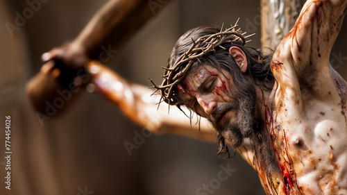Close up image depicts Jesus Christ on the cross, with a crown of thorns and blood on his face and body. He is looking downwards, surrounded by a dark background. Copy space, 16:9