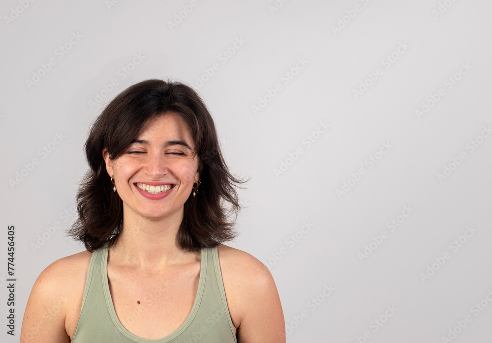 Horizontal portrait of a joyful young woman laughing with closed eyes, isolated on a gray background.