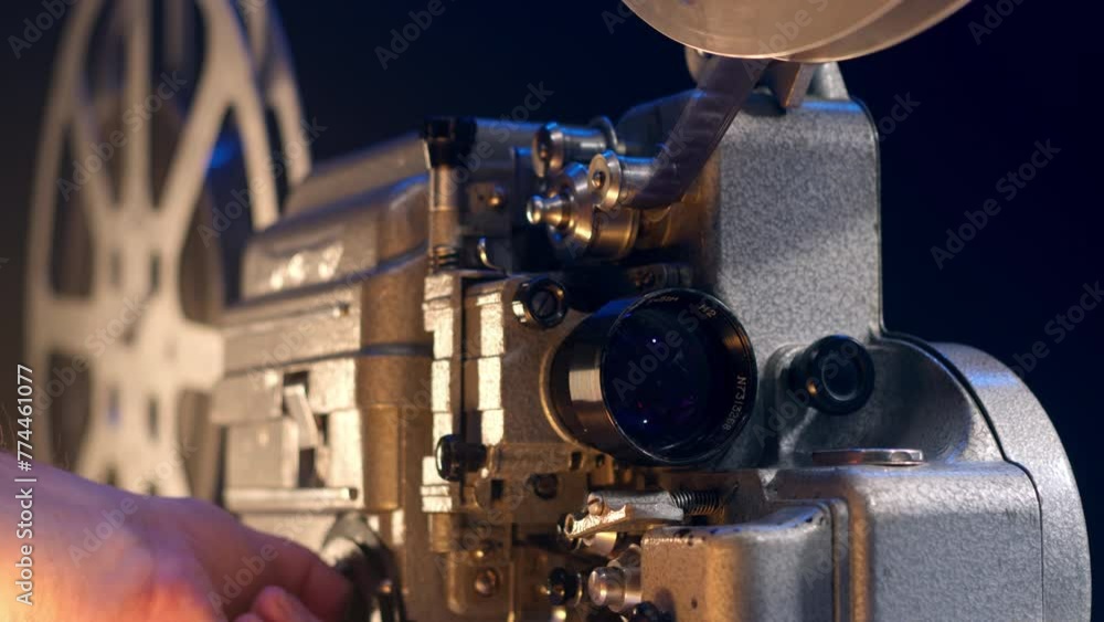 mechanic hand turns on an old vintage 16mm projector for watching a movie in a cinema. The man starts the retro player and the movie starts.