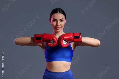 Portrait of beautiful woman wearing boxing gloves in color lights on grey background © New Africa