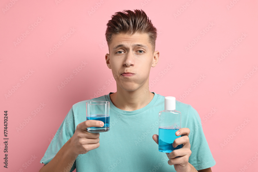 Young man using mouthwash on pink background Young man using mouthwash on pink background