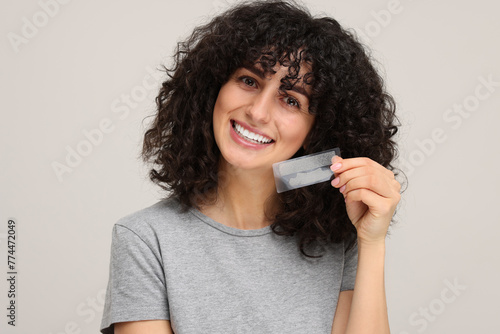 Obraz na plátně Young woman holding teeth whitening strips on light grey background