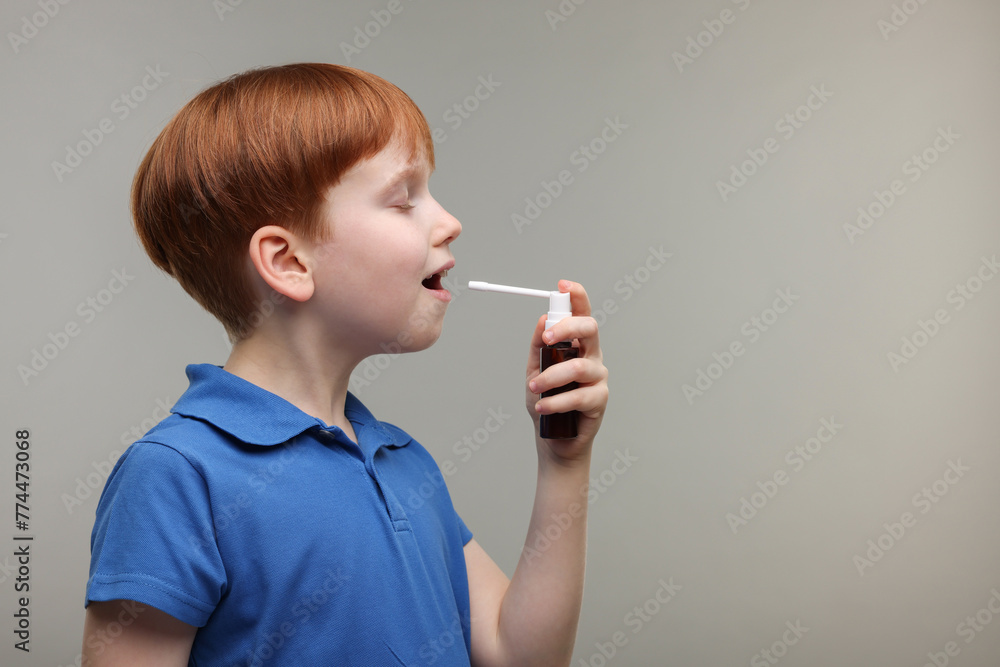 Obraz premium Little boy using throat spray on grey background
