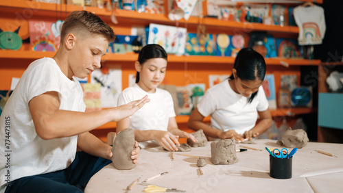 Caucasian smart teenager modeling clay while craving glass of clay at art lesson. Group of multicultural happy student working at dough in pottery workshop. Creative activity concept. Edification.