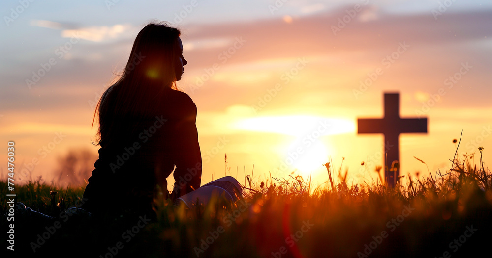 A woman is praying at the cross in the evening sunlight.
