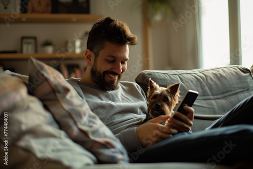 Happy White Man Looking at and Using Smartphone at Home with Cute Dog photo