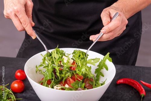 The cook mixes fresh vegetable salad with mozzarella cheese in a bowl, closeup with selective focus
