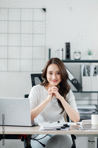 Smiling businesswoman sits confidently at her tidy desk in a modern, well-lit office environment.