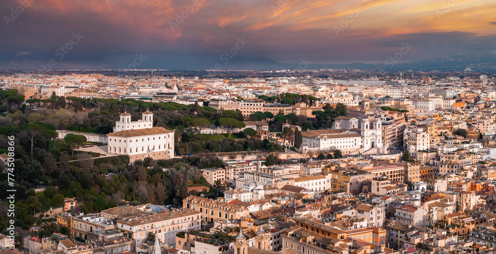 An aerial view of Rome at sunrise or sunset highlights its mix of old and modern buildings under a golden light. Key structures and green areas shine against the urban backdrop, under a vibrant sky.