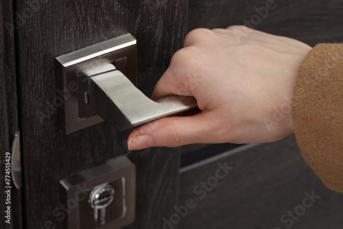 Woman opening wooden door indoors, closeup of hand on handle photo