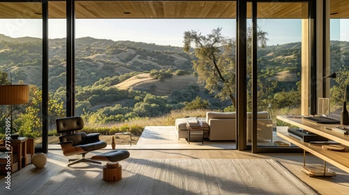 A serene and tranquil home office retreat with a minimalist desk, cozy seating area, and panoramic views of rolling hills and countryside scenery through floor-to-ceiling windows.