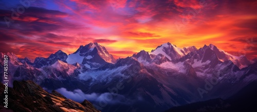 The majestic peaks of a mountain range are silhouetted against a colorful and dramatic sky with scattered clouds