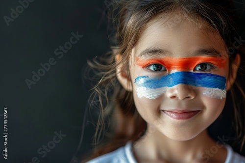 A young girl with blue, white and red paint on her face. Football fan