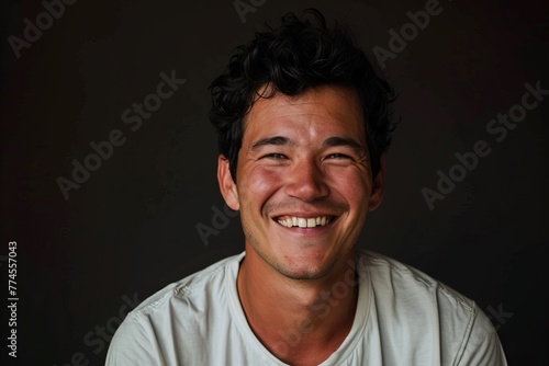 Portrait of a happy young man smiling on a dark background. © Iigo