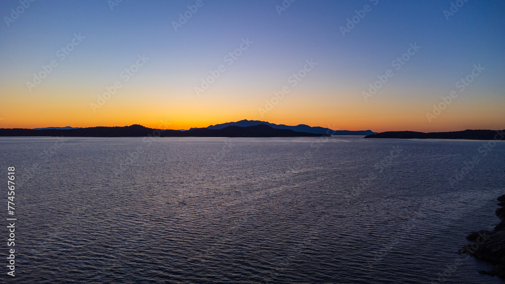 Sunset over Thormanby Island. Yellow glow of sun creeping over the low mountains. 