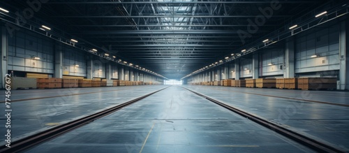 An abandoned warehouse featuring empty train tracks extending towards the horizon under a spacious ceiling