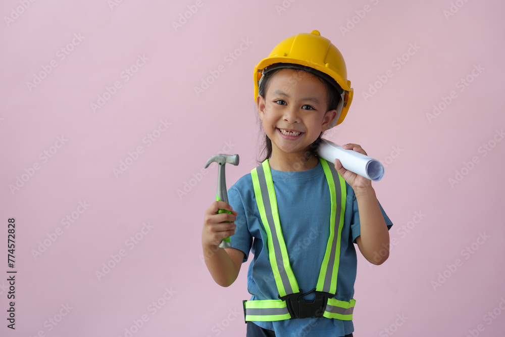A cute girl wearing a yellow construction hat or safety helmet standing on a pink background holding a blueprint. Construction equipment, design, future career concepts, engineers, architects. A cute girl wearing a yellow construction hat or safety helmet standing on a pink background holding a blueprint. Construction equipment, design, future career concepts, engineers, architects.