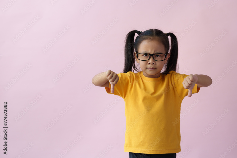 Fototapeta premium Little girl wearing glasses suffering from headache, hopeless, angry, and stressed because of pain and migraine, hands on head, tired, standing on pink copy space background.