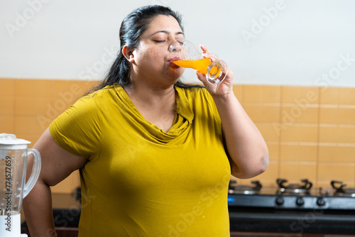 Overweight fat indian woman drinking a fruit juice in a kitchen.healthy eating concept.