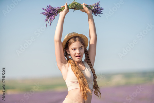 girl is holding a bunch of lavender purple flowers in her hands and wearing a straw hat. She is smiling and she is enjoying herself. 