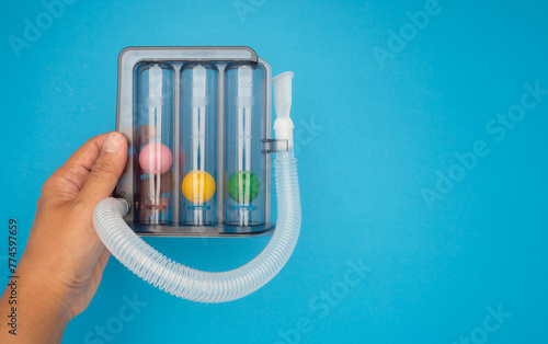 Incentive spirometer. Hand holding a respiratory lung exerciser against a blue background. photo