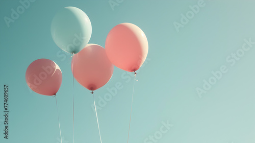 Pink, blue and green balloons floating in the sky. The balloons are tied together and are scattered in the air. The sky is clear and blue, creating a peaceful and serene atmosphere