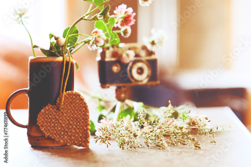 Vintage style, analogue camera on the table and summer flowers in the cup with heart. Summer or Autumn season concept. Fall, thanksgiving, love, travel concept. Home sweet home