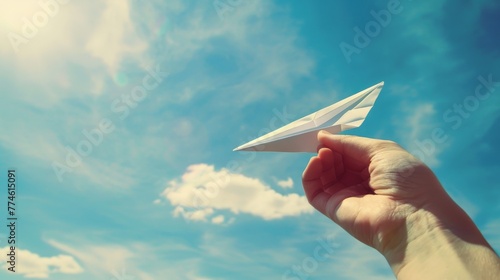 a hand holding a paper plane against a blue sky