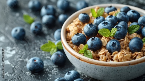  A bowl of oatmeal topped with blueberries and mint sprigs, placed on a gray background with some additional blueberries strewn nearby