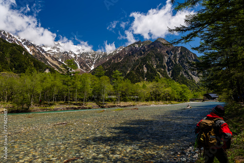 Hiker next to a clear, fast flowing river in front of snowcapped mountain peaks
