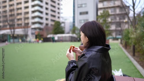 A Japanese woman in her 20s eating churros sitting in a park around Gotanda Station in Shinagawa-ku, Tokyo in winter 冬の東京都品川区五反田の駅周辺の公園に座ってチュロスを食べる20代の日本人女性 photo