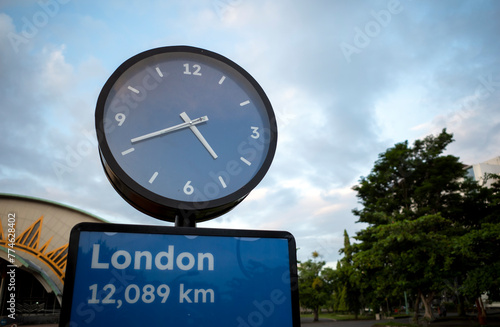 A blue traffic sign board of London and a blue public clock, 12089 km from London.