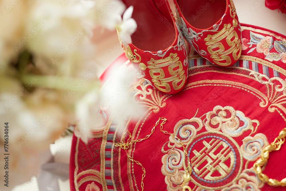 A pair of red and gold embroidered shoes rests on matching fabric, adorned with intricate patterns