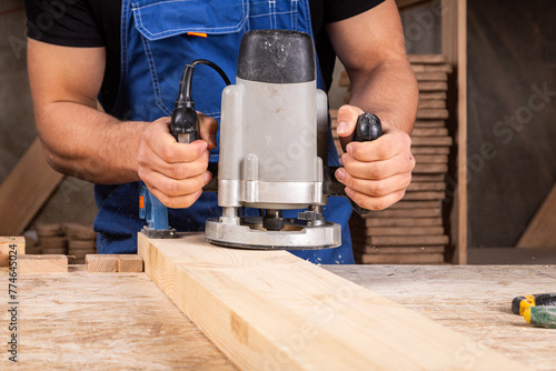Male carpenter using electric sander to polish wooden plank in joinery workshop