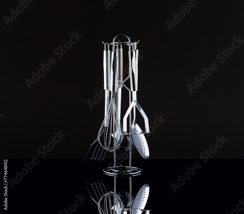 set of kitchen tools on a black background. spatula, whisk, slotted spoon made of stainless steel. studio shot