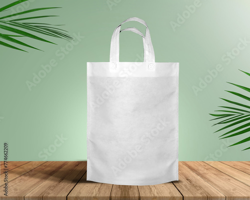 White Color Eco Friendly Tote Bag With Loop Strap. Non Woven Fabric Bag isolated on wood table with plants green background With copyspace for text photo