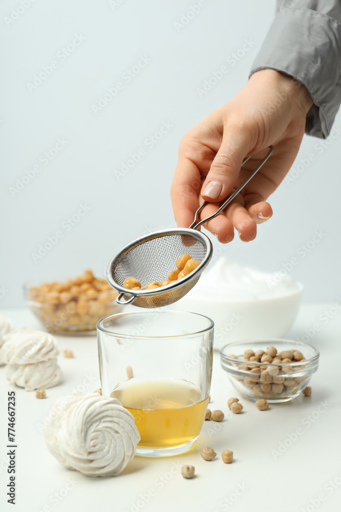 Marshmallows, chickpeas, jar of aquafaba and sieve in hand on white background Marshmallows, chickpeas, jar of aquafaba and sieve in hand on white background