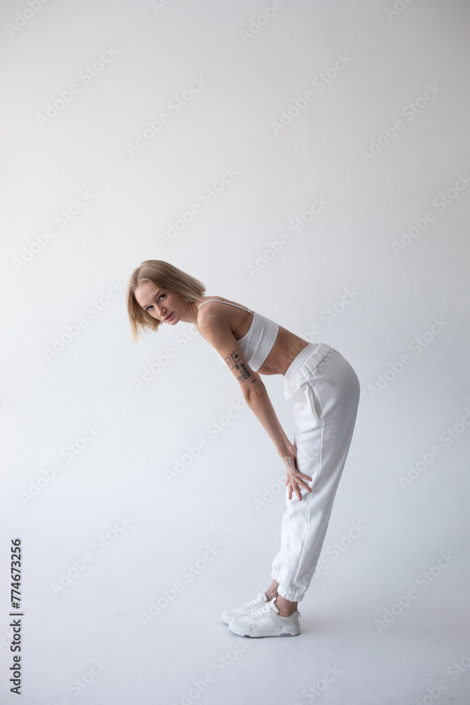 Beautiful blonde girl in a white top and tights posing on a white background Beautiful blonde girl in a white top and tights posing on a white background