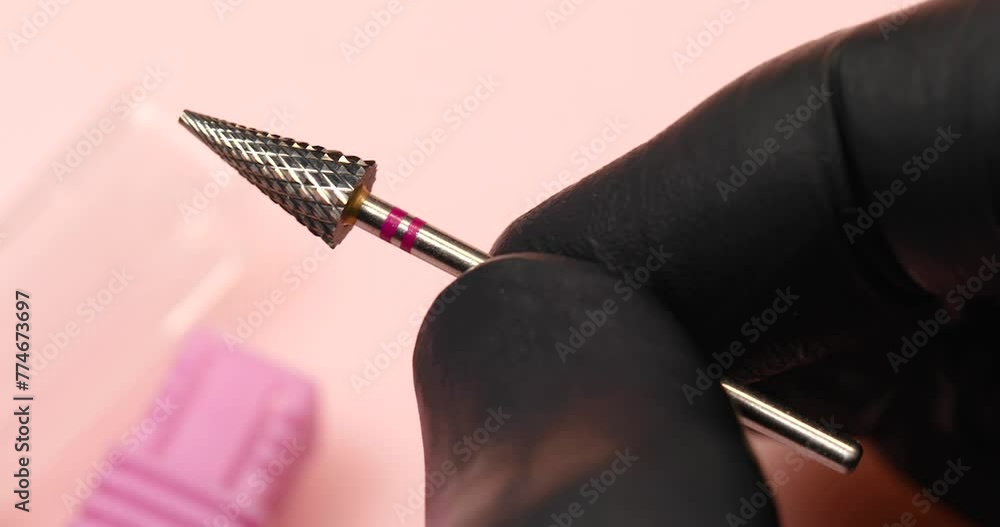A specialist holds in his hands a carbide cutter for hardware manicure with a red notch on a pink background, close-up