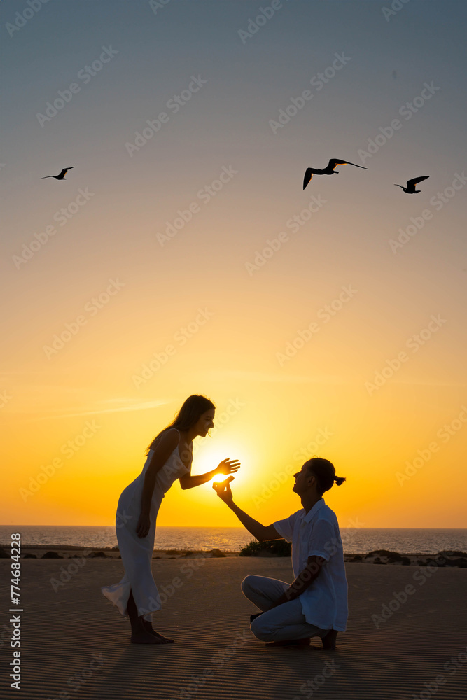 Fototapeta premium Silhouette of a couple during a marriage proposal on the beach with a beautiful sunset backdrop