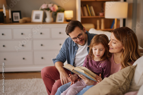 Family with little daughter reading book on sofa in living room