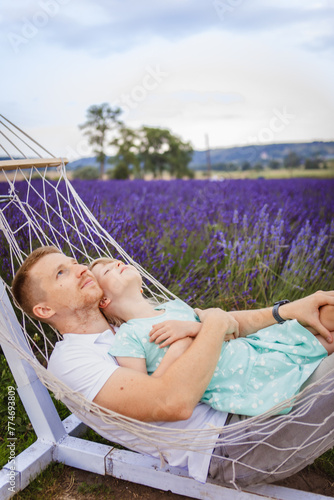 father and daughter lie in a hammock. lavender field in the background © phpetrunina14