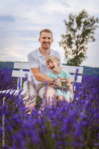 father and daughter are sitting on a bench in a lavender field © phpetrunina14