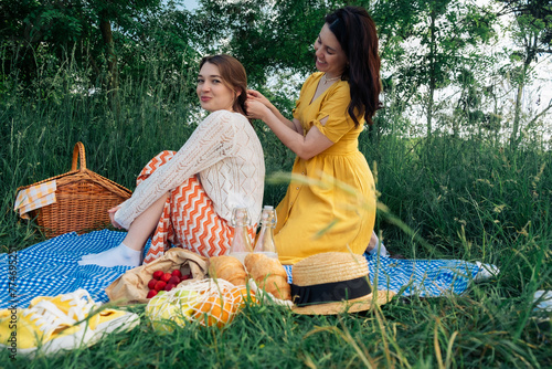 Two girls on a date sit on a blue blanket for a picnic in nature © phpetrunina14