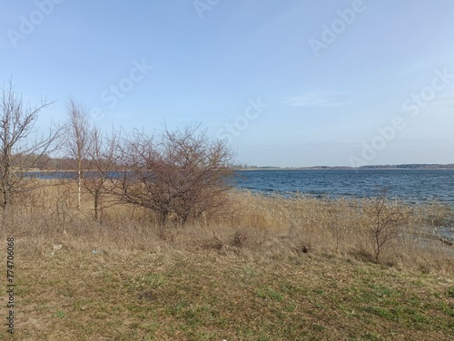 Gudeliai lake and lakeshore during sunny day. Lake with small waves. Lake shore with grass and reeds growing on it. Sunny day with white and gray clouds in blue sky. Nature. Gudeliu ezeras. photo
