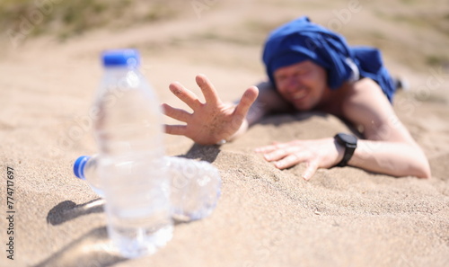 Obraz na plátně Dehydrated man crawling on sand for bottle of drinking water closeup