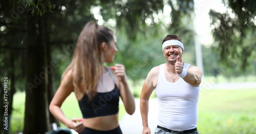 Man in park shows ok gesture to sports girl. Running has beneficial effect on respiratory system body. Happy girl looks at man who smiles at her. Classes relieves stress and uplifting.