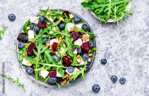 Healthy useful salad with beetroot, blueberries, feta cheese, arugula and walnuts, gray table background, top view
