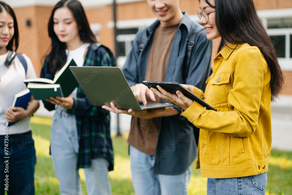 Young college students is reading a book while relaxing sitting on grass in a campus park with her friends. Education concept in morning Young college students is reading a book while relaxing sitting on grass in a campus park with her friends. Education concept in morning